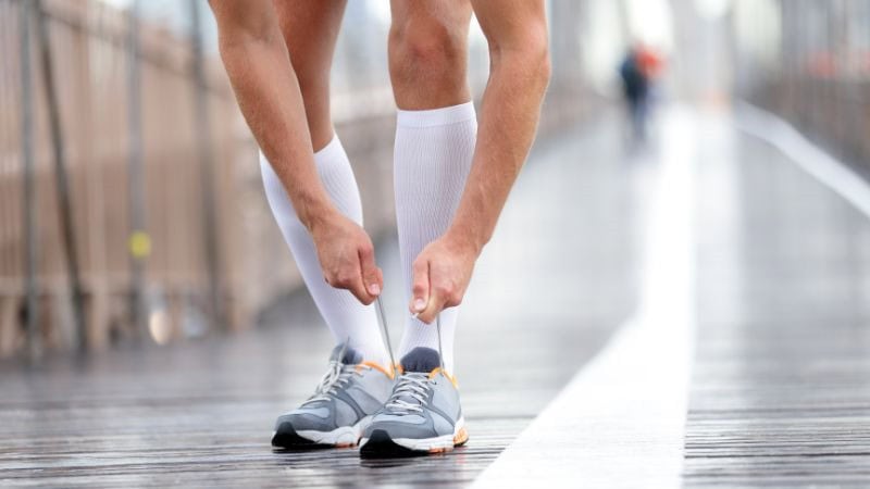 A man wearing wicking socks is tying his shoelaces.