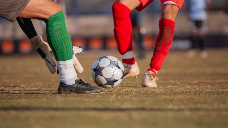 Two athletes wearing football socks fighting for a football