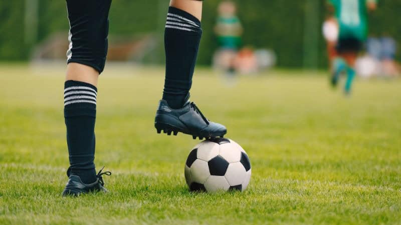 A referee wearing black football socks controls the football
