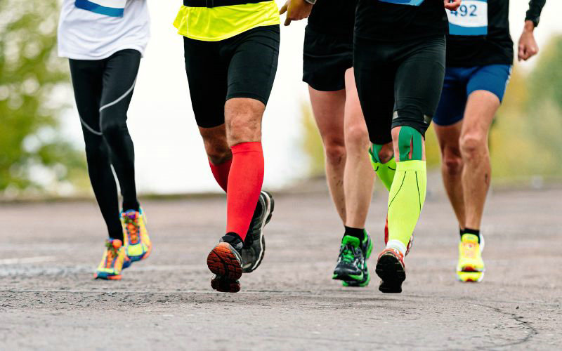 Group of runners competing in a race, focusing on their legs clad in colorful compression socks and running gear, captured on a cloudy day on a wet road.