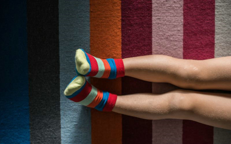 A child's legs in colorful striped socks rest on a multicolored striped rug.