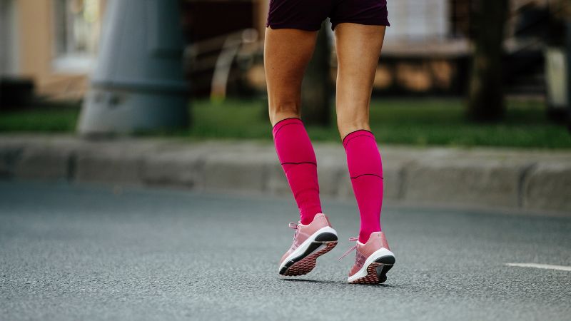 Un joggeur portant des chaussettes roses Sinoknit jusqu'aux genoux et des chaussures de course garde ses pieds confortables sur une route pavée.