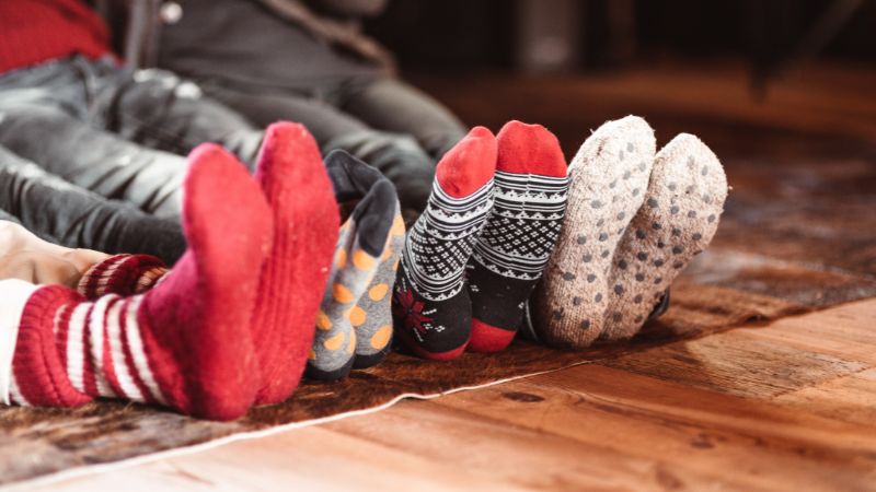 Vijf paar voeten in kleurrijke, vochtafvoerende sokken staan op een houten vloer, zodat ze de hele dag droog en comfortabel blijven.