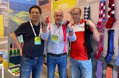 Three men stand at a booth showcasing colorful socks at an event.