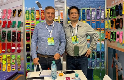 Two men in a trade show booth, surrounded by colorful socks on display.