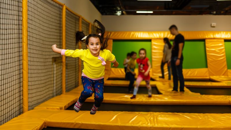 A child in a yellow shirt happily jumps on a trampoline at a vibrant USA park, joined by others in the lively play area.