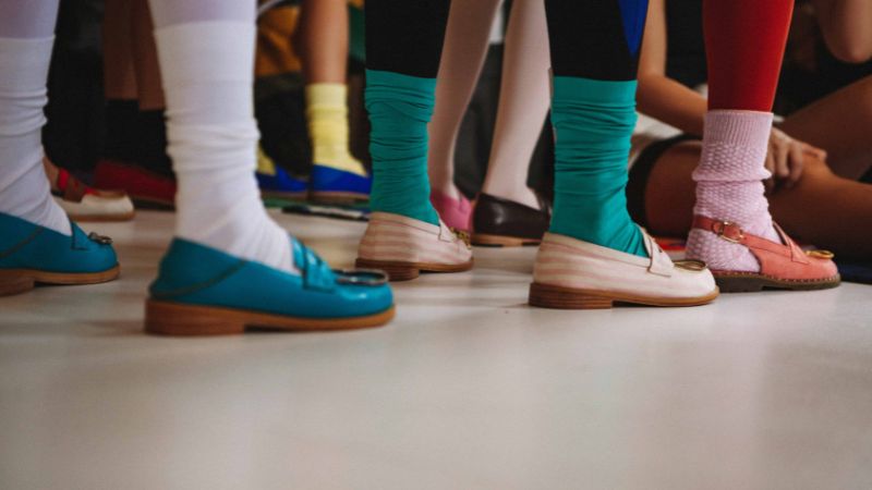 A group wearing vibrant Sinoknit socks and stylish loafers stands on a light floor.