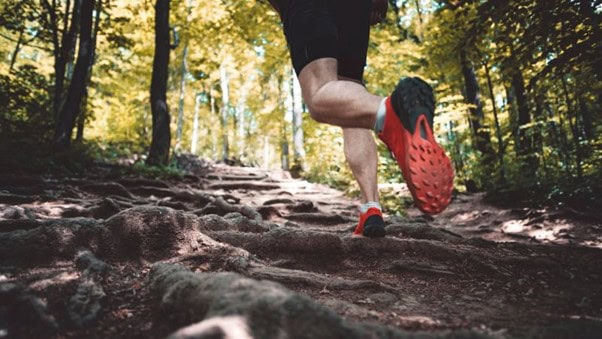 Una persona corriendo por un sendero forestal rocoso con zapatos de suela roja.