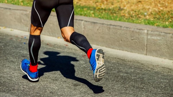 Seorang pelari dalam legging hitam dan kasut biru dengan aksen merah menggunakan stoking mampatan untuk mengelakkan shin splint.