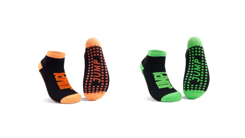 Two pairs of "JUMP" ankle socks with grips: black/orange and black/green. Perfect for trampoline safety and active play.