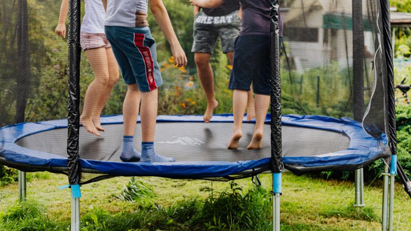 Kids joyfully bouncing on a trampoline with a safety net outdoors.