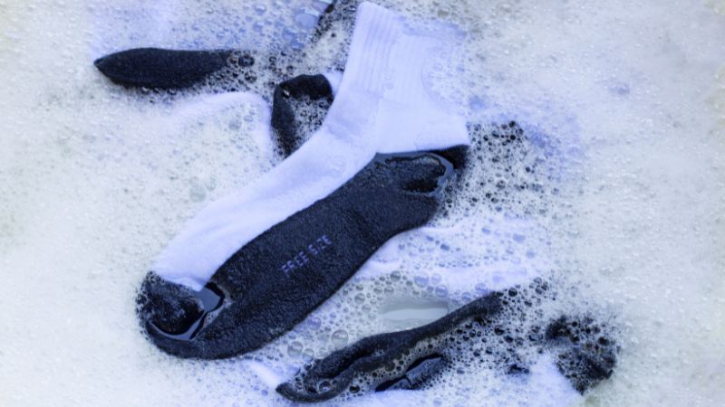 Black and white Wash Grip Socks soak in soapy water, with bubbles dancing on the surface.