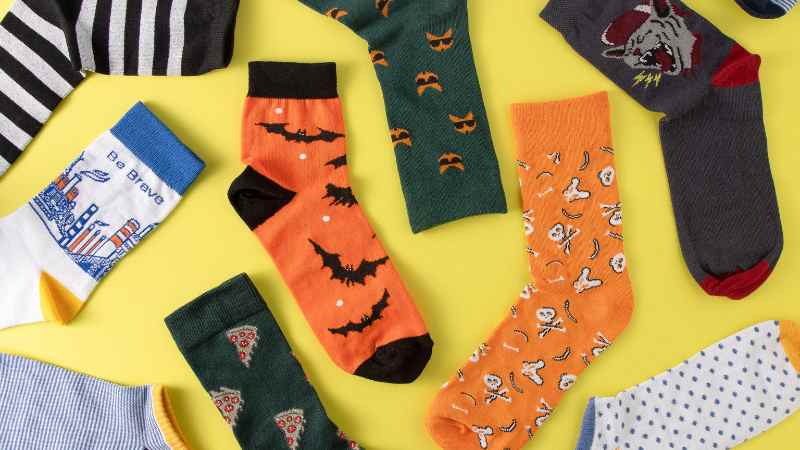 Colorful Halloween-patterned socks scattered on a yellow background, perfect for keeping your feet cozy.