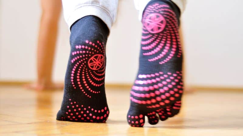 Person wearing black grip socks with red dots stands on a wooden floor indoors—great DIY grip sock inspiration.