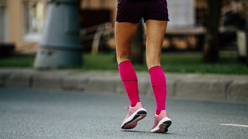 Bright pink compression socks worn during running or walking exercises; athletic footwear on a person's legs on a city street.