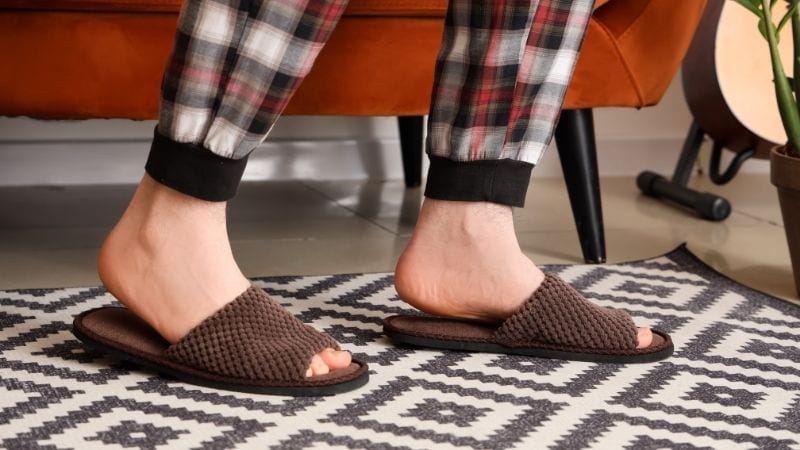 Comfortable brown plush slippers on a person's feet, casual home setting with a patterned rug, relaxing lifestyle, cozy indoor ambiance, perfect for comfy home footwear.