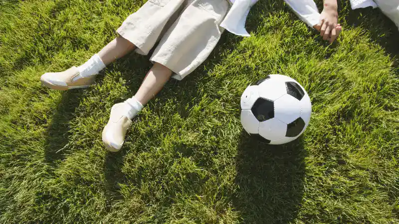 Person wearing white sneakers and ankle socks lying on grass with a soccer ball, suitable for casual summer sportswear.