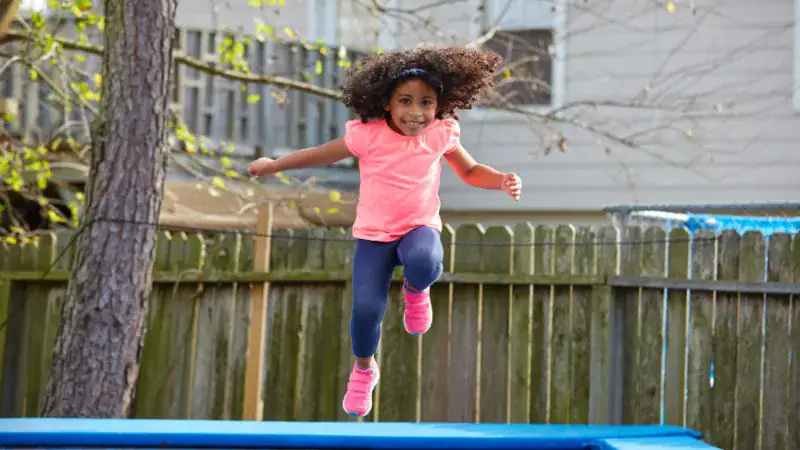 Child jumping on trampoline wearing socks in backyard, enjoying active play.