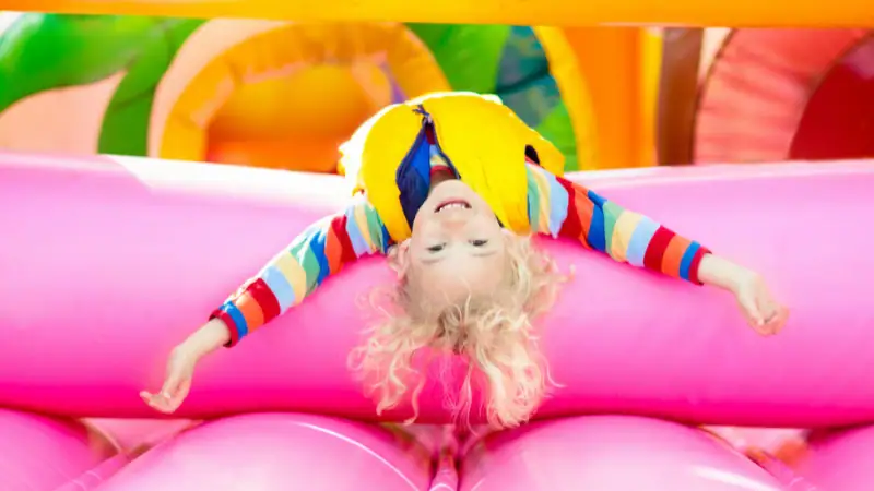 Child lying upside down on a colorful trampoline, wearing socks, enjoying outdoor play.
