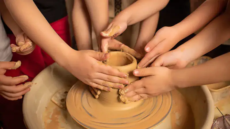 Pottery wheel with hands shaping clay, emphasizing craftsmanship and collaborative art.