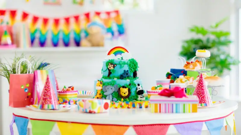 Rainbow-themed birthday cake with vibrant colors, playful animal toppers, and festive party accessories for a joyful celebration.