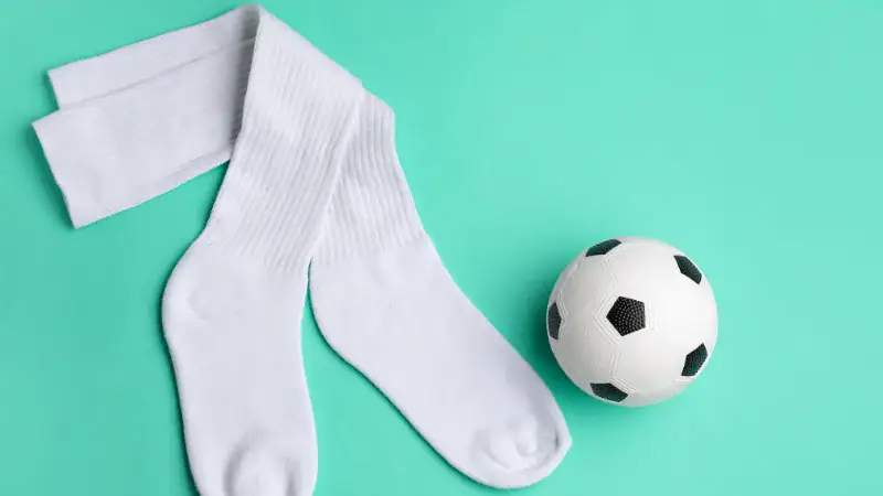 High-quality white sports socks with ribbed texture next to a classic black and white soccer ball on a mint green surface.